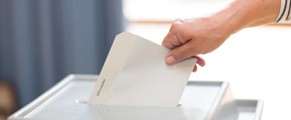 Hand wirft Stimmzettel in Urne