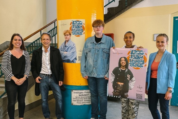 5 Menschen stehen vor einer Säule, wo das Plakat zur Kampagne hängt.