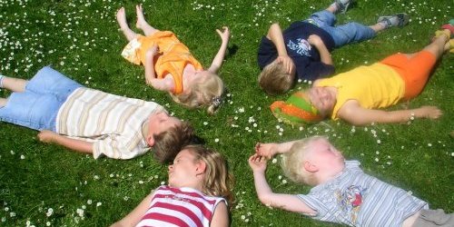 Kinder liegen mit geschlossenen Augen im Kreis auf einer Wiese
