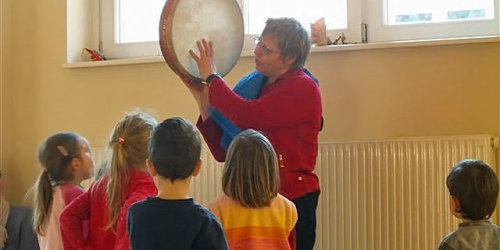 Eine Frau zeigt Kindern wie man auf einer Trommel spielt.
