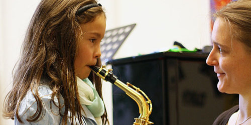 Eine Lehrerin bringt einem kleinen Mädchen das Saxophon spielen bei.