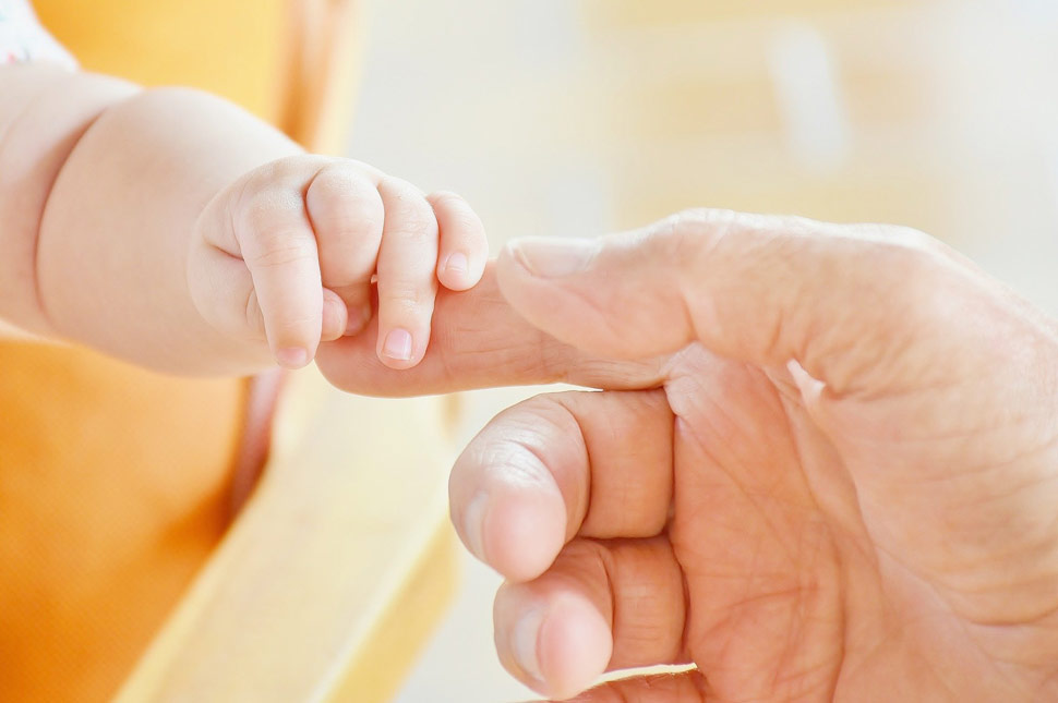 Die Hand eines Säuglings greift nach der Hand eines Erwachsenen und umschließt einen Finger.