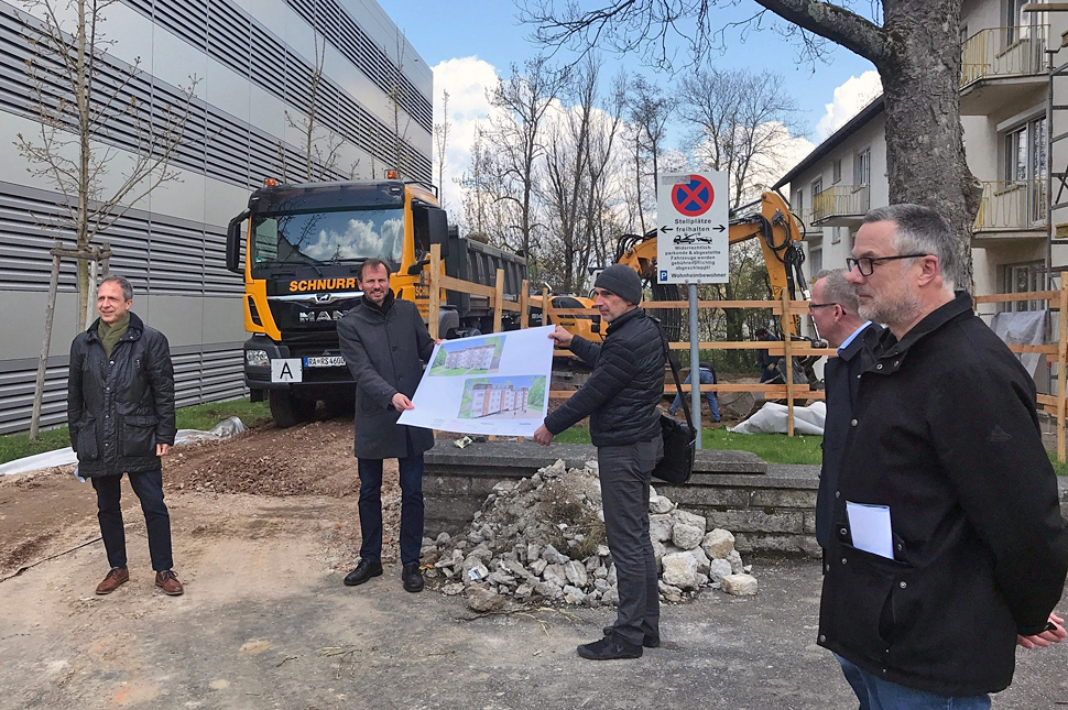 Bürgermeister Roland Kaiser mit Alexander Wieland, Martin Wurz, Sven Pries und Wolfgang Schoch (von links). Alexander Wieland und Martin Wurz halten ein Plakat mit einer Ansicht der Häuser. Im Hintergrund steht ein Bagger und ein LKW.