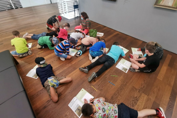 Kinder liegen auf dem Boden und beschriften Hefte