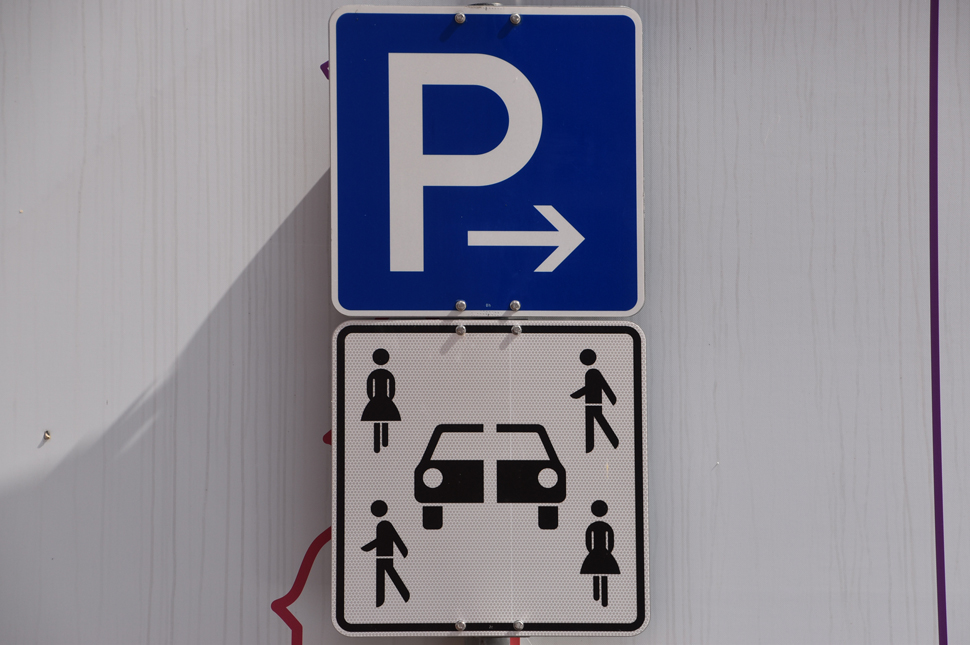 Das neue Car Sharing Schild zeigt ein Auto, das in der Mitte geteilt und mehrere Menschen daneben. Darüber ist ein blaues Parkplatzschild. 