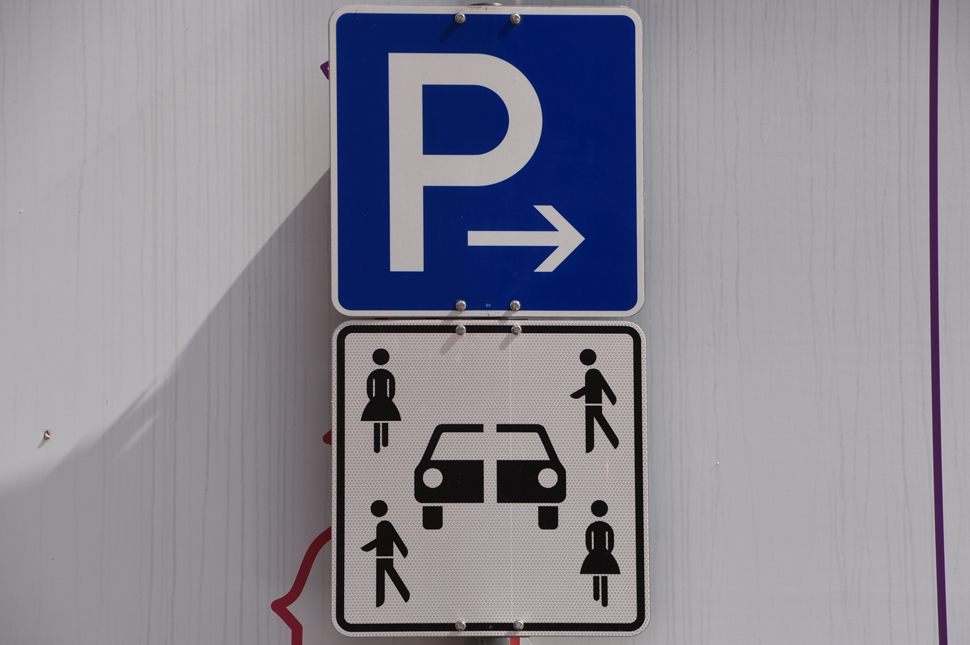 Das neue Car Sharing Schild zeigt ein Auto, das in der Mitte geteilt und mehrere Menschen daneben. Darüber ist ein blaues Parkplatzschild.