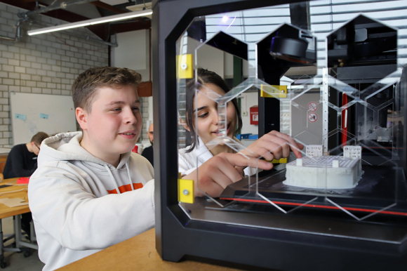 Schüler und Schülerin arbeiten an einem 3D-Drucker