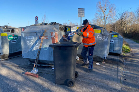Ein Müllwerker räumt an einem Glascontainer-Platz wild heurmliegenden Müll auf. 