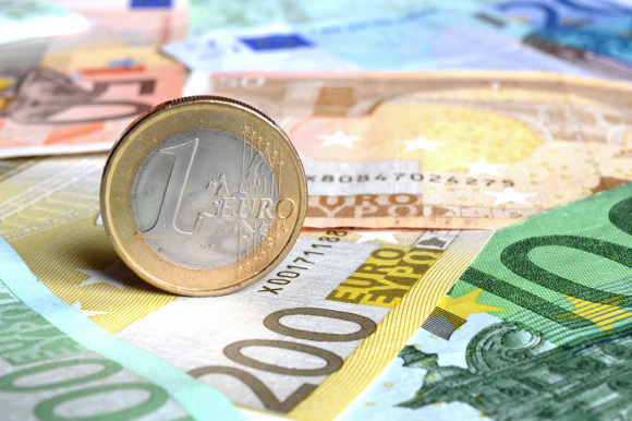 Eine Euro-Münze stehend auf Euro-Geldscheinen