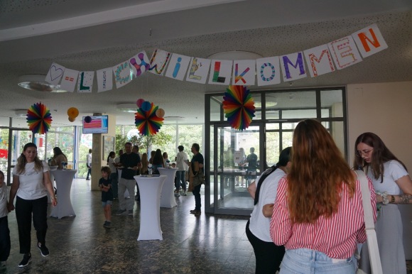 In der Aula der Realschule stehen verschiedene Personengruppen. 