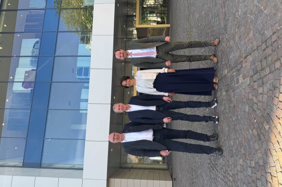 Drei Männer und eine Frau stehen sehr gut gekleidet in einer Reihe vor dem Kongresshaus.