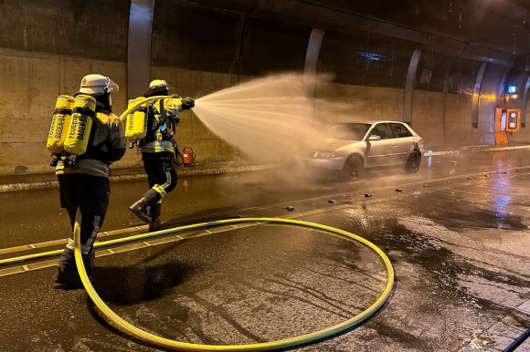 Zwei Feuerwehrmänner löschen ein Auto in einem Tunnel.