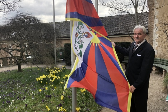 Oberbürgermeister Späth steht an einem Fahnenmast und hält die Tibet-Flagge in der Hand.