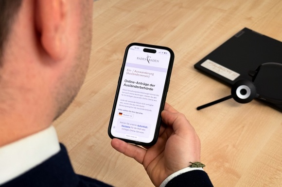 Blick über die Schulter eines Mannes, der ein Smartphone in seiner Hand hält.