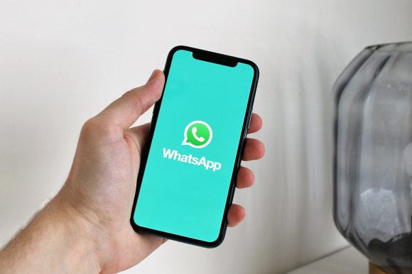 Hand hält Smartphone. Auf dem Smartphone ist WhatsApp geöffnet.