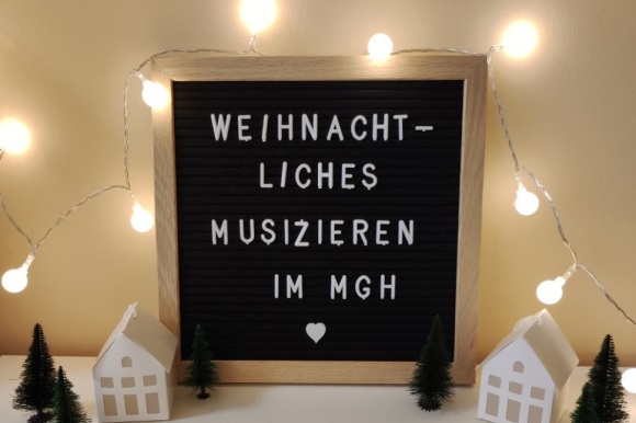Tafel mit Lichterketten, auf der steht "Weihnachtliches Musizieren im MGH".