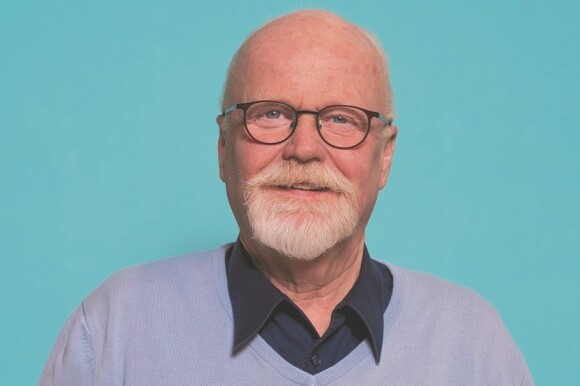 Ein Mann mit Brille steht vor einem hellblauen Hintergrund.