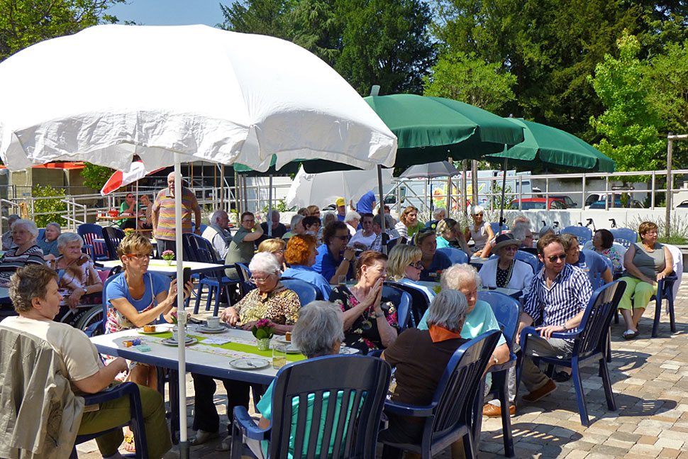 Menschen verschiedenen alters sitzen bei einem Hoffest unter Sonnenschirmen
