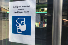 Plakat an einer Bustüre: Grafik eines Menschen mit Mundschutz, darüber steht "Zustieg und Aufenthalt nur mit Mund-Nasen-Schutz".