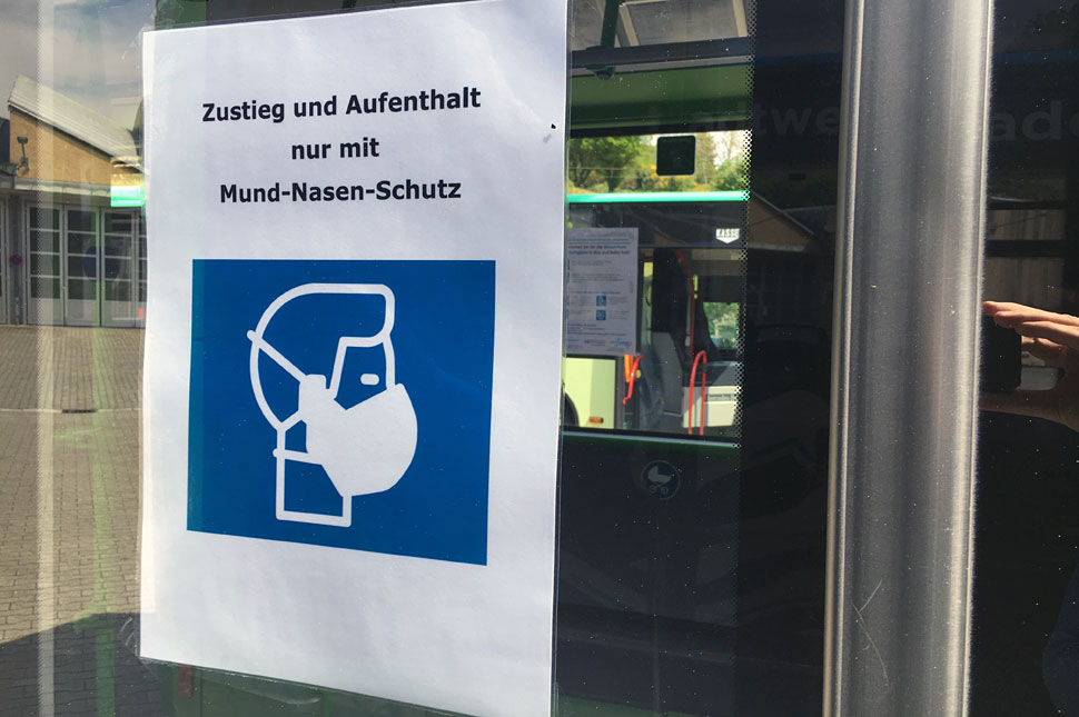 Plakat an einer Bustüre: Grafik eines Menschen mit Mundschutz, darüber steht "Zustieg und Aufenthalt nur mit Mund-Nasen-Schutz".