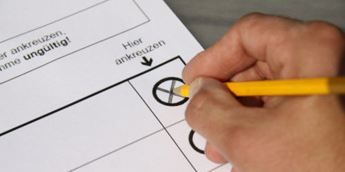 Hand mit Stift kreuzt einen Wahlschein an