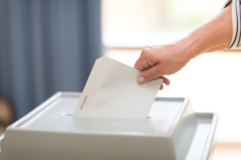 Hand wirft Stimmzettel in Urne