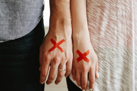 Hand von einem Mann und einer Frau. Der Mann trägt einen Ehering. Auf beiden Händen ist ein großes, rotes Kreuz zu sehen.