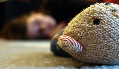 Ein Teddybär liegt am Boden, im Hintergrund eine Frau.