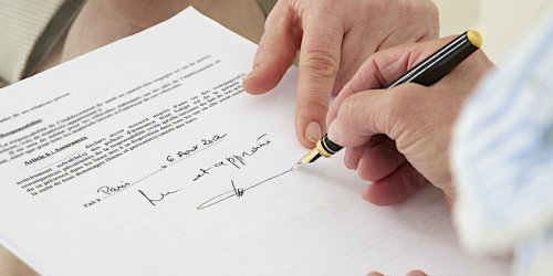 Eine alte, zebrechliche Hand unterschreibt ein Dokument.