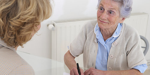 Eine Seniorin wird von einer Frau beraten und unterschreibt ein Dokument.