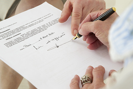 Eine alte, zebrechliche Hand unterschreibt ein Dokument.