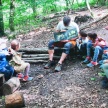Kinder sitzen im Wald um ein Lagerfeuer. 