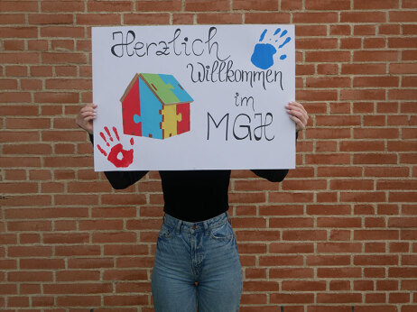Eine Frau hält ein Schild in die Höhe, auf dem steht "Herzlich Willkommen im MGH".