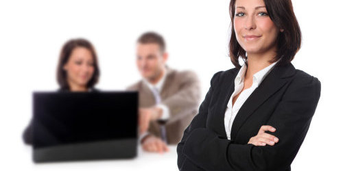 Frau im Business-Look, im Hintergrund die gleiche Frau und ein Mann an einem Laptop