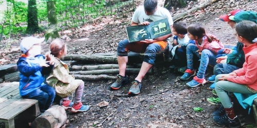 Kinder sitzen im Wald um ein Lagerfeuer. 