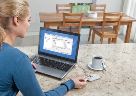 Junge Frau sitzt am PC mit neuem Personalausweis und digitalem Lesegerät