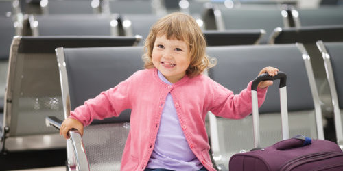 Ein Kleinkind sitzt auf einem Stuhl und hält einen Koffer in der Hand.