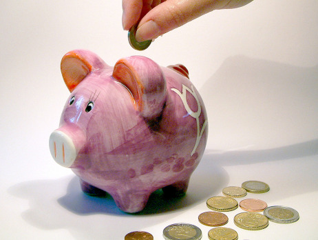 Eine Hand wirft Münzen in ein rosa Sparschwein