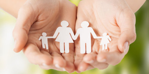 Zwei Hände halten eine Familie aus Papierfiguren