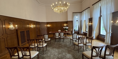 Großer Tisch in der Mitte des Trausaales, dahinter stehen Stühle aufgereiht.