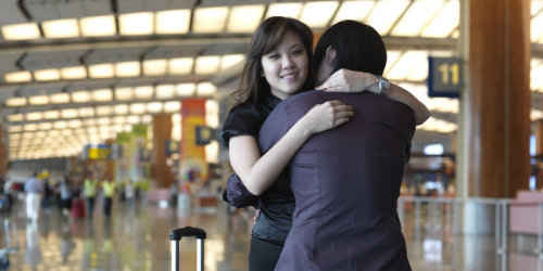 Ein chinesischer Mann und eine chinesische Frau umarmen sich an einem Bahnhof. Neben der Frau steht ein Koffer.