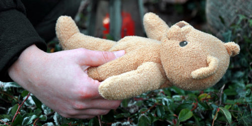 Eine Hand legt einen Teddybären auf ein Grab