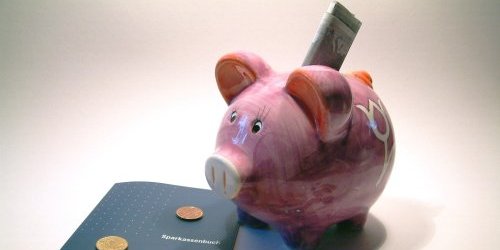 Ein Sparschwein in dem ein Geldschein steckt. Nebendran ein Sparkassenbuch Geldscheine und Münzen