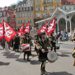 Mehrere Männer traditionell gekleidet spielen auf einer Parada mit ihren Trommeln. Im Hintergrund mehrere Fahnenschwenker.