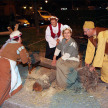 Bernhardusfest. Eine verkleidete Frau sitzt auf einem Baumstamm während zwei weitere Frauen in gemeinsam Sägen. Ein Männ steht daneben und hebt den Baumstamm.