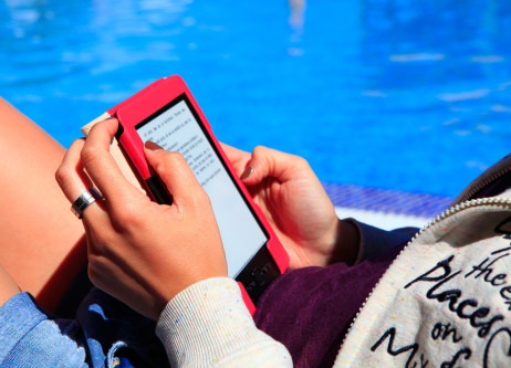 Frau sitzt im Sommer am Pool und liest auf einem eBook Reader