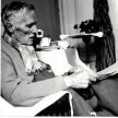 Otto Flake sitzend, hält ein Buch in der Hand. Links neben ihm ein Tisch mit Kaffeegedeck