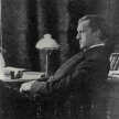 Otto Falke sitzt auf einem Stuhl an seinem Schreibtisch. Ist im Profil zu sehen