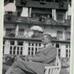 Otto Flake sitzt auf einer Bank. Seitliches Profil mit Zigarette in der Hand. Im Hintergrund ein Ferienhaus