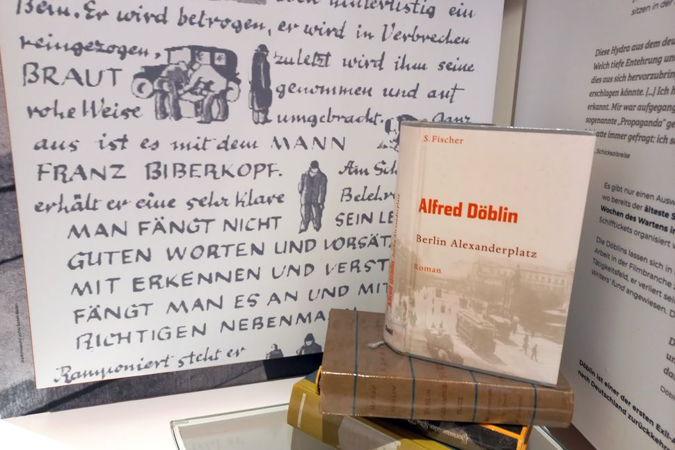 Buch auf Bücherstapel aufgestellt. Im Hintergrund sind Teile des Museumsbereichs zu Alfred Döblins Alexanderplatz zu sehen.